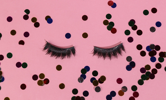 Minimal beauty, party layout. False eyelashes with confetti on a pink background. Top view