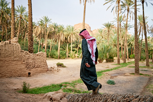 Full length view of young Middle Eastern man in lush environment, for centuries a popular resting place along trading route on west side of Arabian Peninsula.