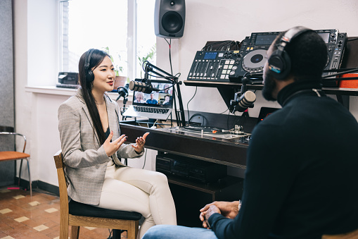 Young woman and mid adult man recording a podcast in their studio.