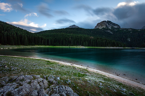Twilights over the Black lake at Montenegro. Emerald water of the lake under the sky blurred in motion and dark silhouettes of the woods and mountain
