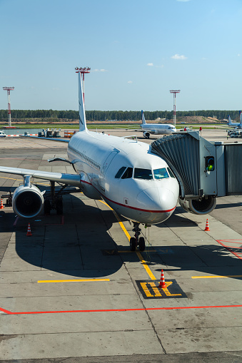 Passenger airplane on the airfield docked with passenger boarding bridge. Preparations of the airplane at the airport terminal.