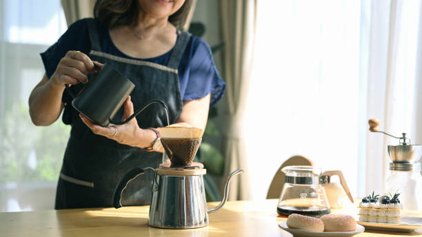istock Middle aged woman standing at kitchen table, brewing drip coffee and enjoys her morning. 1401478586