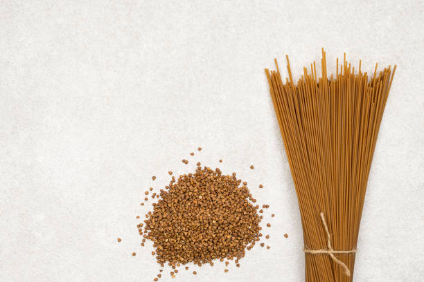 bunch of brown long spaghetti and buckwheat on grey background.