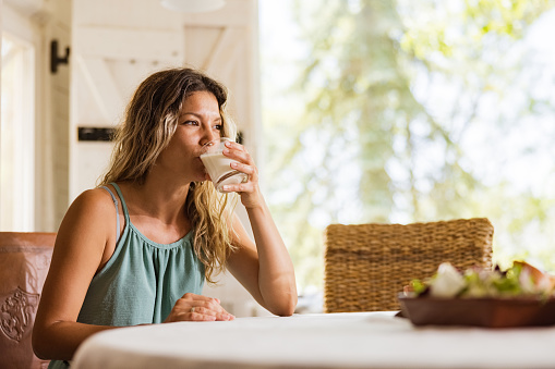 Mid adult woman drinking yogurt during morning in dining room.