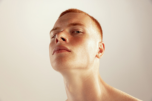 Close-up portrait of young red-haired freckled man posing isolated over grey studio background. Concept of men's health, lifestyle, beauty, body and skin care. Model looking at camera