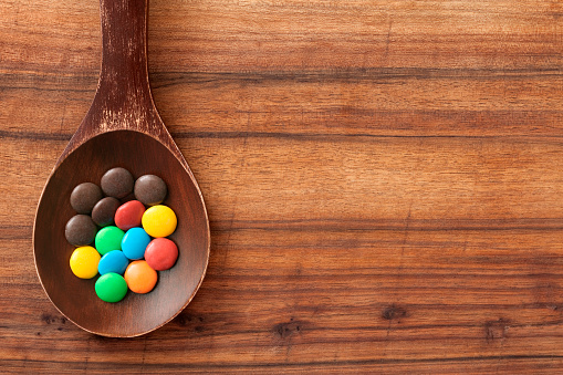 Top view of wooden spoon over table with multi colored chocolate candies on it