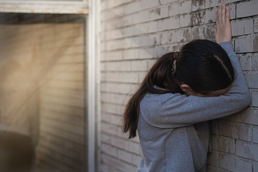 A young woman standing against a brick wall. Hiding her face against the wall. Depressed girl having a melt down. Emotional distress, unhappy, negativity, problems.