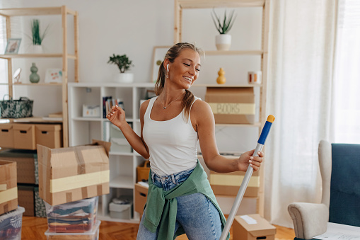Beautiful scandinavian descent young woman cleaning the house and dancing at the same time