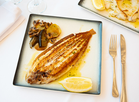 Delicious roasted black sole fish served with stewed vegetables and fresh lemon seasoned with aromatic herbal oil