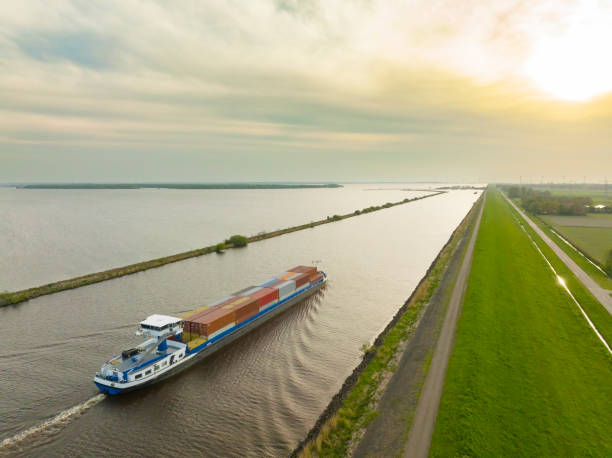 Container ship barge sailing on a canal Container ship barge sailing on the Ramsdiep canal in Flevoland, Netherlands towards the IJsselmeer. The ship is carrying multiple containers stacked on the deck of the ship. barge stock pictures, royalty-free photos & images