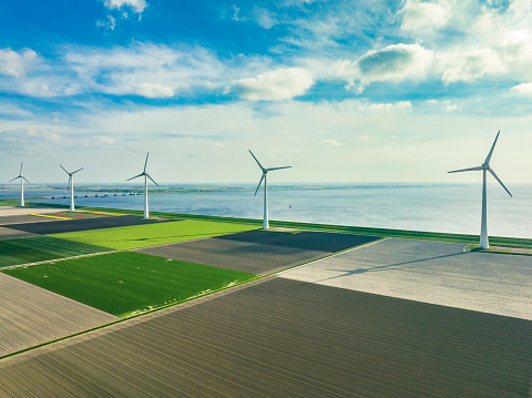 Wind turbines next to a levee on the shore of the IJsselmeer in the Noordoostpolder in Flevoland, The Netherlands, during springtime seen from above. The Noordoostpolder is a polder in the former Zuiderzee designed initially to create more land for farming.