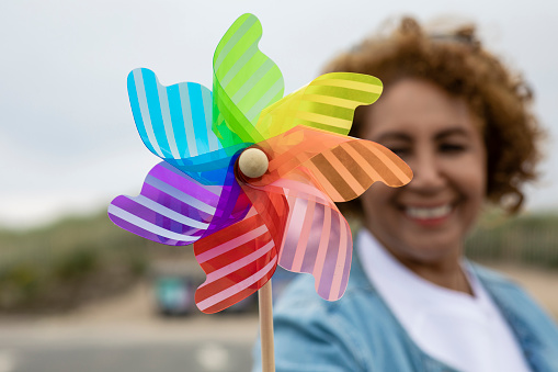 A senior woman holding a pinwheel toy towards the camera at Beadnell beach, North East England. She is out of focus and is smiling while looking at the camera.