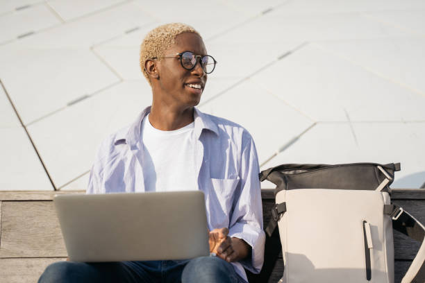 istock Smiling African American freelancer using laptop computer looking away . Stylish business man wearing eyeglasses working online outdoors, copy space. Successful business 1401495173