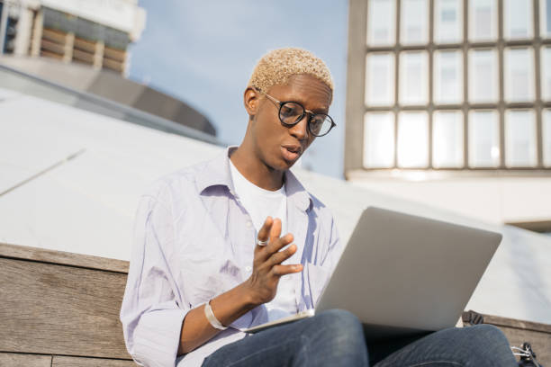 istock African American student studying, using laptop computer, having online lesson sitting outdoors. Freelancer wearing stylish eyeglasses communication using wireless technology. Video conference 1401495177