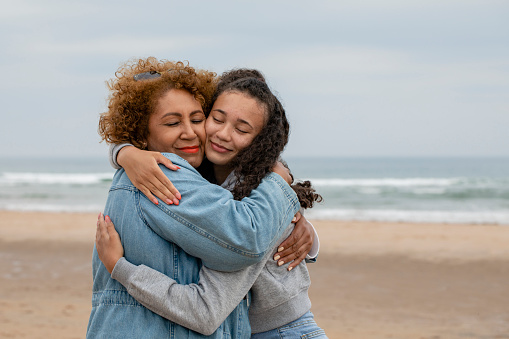 A senior woman standing on the beach at Beadnell, North East England with her granddaughter. They are hugging each other cheek to cheek.