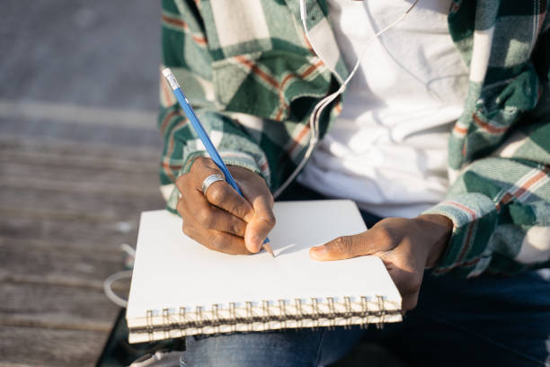 Artist hand drawing sitting outdoors, selective focus. Writer taking notes into paper notepad stock photo