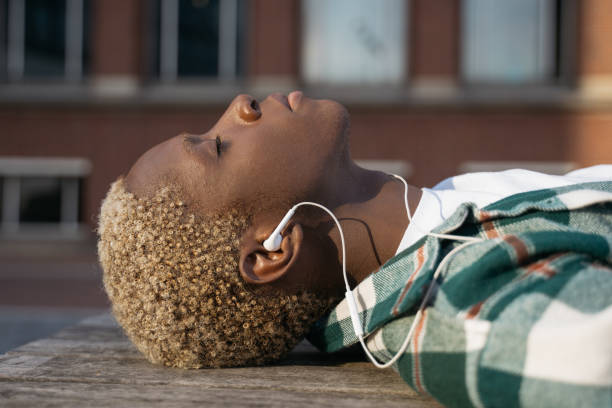 Stylish African American man relaxing, listening music with closed eyes lying on the street, selective focus stock photo