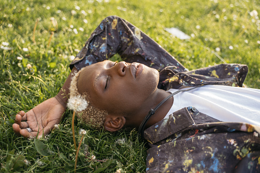 Portrait of young African American guy with stylish hair laying on grass, relaxing in park. Fashion model posing for pictures. Beauty concept