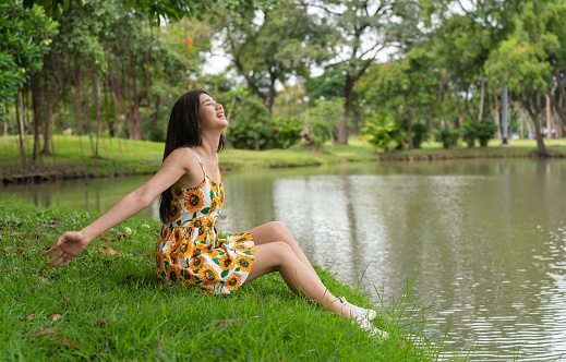 Photograph of a young asian lady enjoying the breeze while chilling and relaxing in a park.