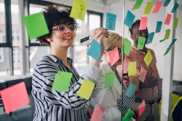 Photo of Multiracial team at work writing ideas on sticky notes on the glass wall
