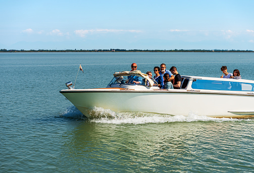 Venice, Italy - June 2, 2021: Water taxi in motion in the Venetian lagoon with a group of people on board, on a sunny spring day. UNESCO world heritage site, Venice, Veneto, Italy, Europe. This mode of transport is certainly the fastest way to move around the city of Venice to the islands of the Venetian lagoon.