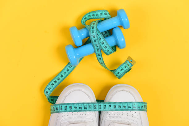 istock Sneakers with measuring tape on yellow background. 1401499761