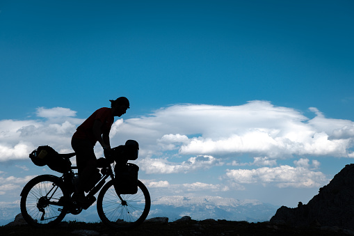 High altitude silhouette shot.Bike tour with camp.Clouds sky blue in the background.One of 30 shills on the bike is in motion.Bikepacking style bags on the bike