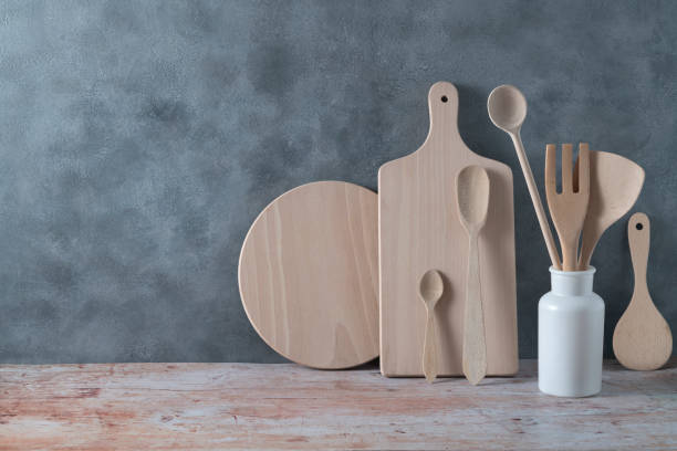 Modern kitchen kitchenware in light wood color with ladle, cutting boards and cookware on gray Modern kitchen kitchenware in light wood color with ladle, cutting boards and cookware on contemporary gray cement wall kitchenware shop stock pictures, royalty-free photos & images