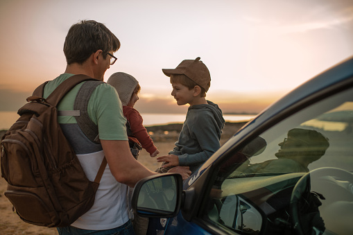 Family near a car watching sunset over the sea