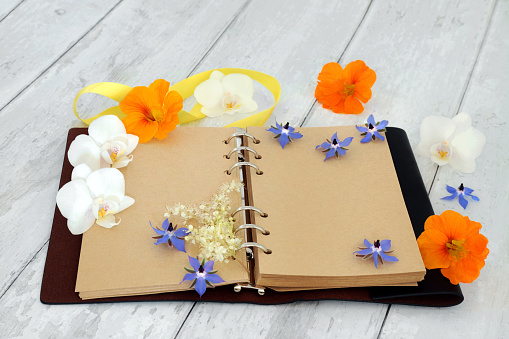 Leather bound journal or diary with blank pages for personal notes or story, with orchid flowers, nasturtium and borage herb flowers. On rustic wood background.