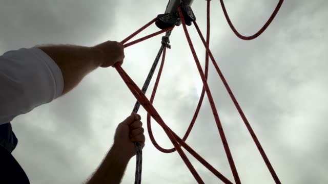 The sailor energetically pulls and secures a rigging rope with a pulley system on a boat.