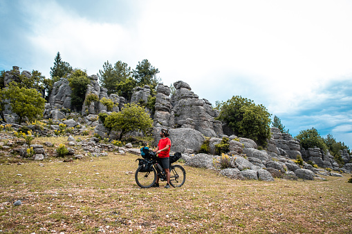 Cyclist in red top helmet rides on terrain among different rock formations and looks around with admiration.Cloudy weather