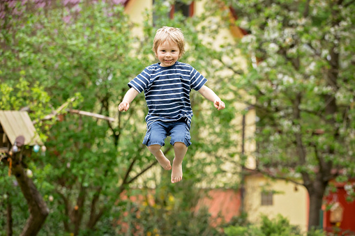 Child, jumping high on a trampoline in backyard
