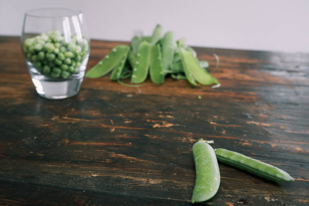 green peas in glass bowl. fresh pea in the pod with green leaves. green peas on a brown wodden table - green pea pea pod salad legume imagens e fotografias de stock