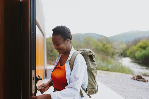 Photo of a young woman unlocking and entering a vacation home she has rented. She is renting a cabin by the river, quiet and secluded from city hustle.
