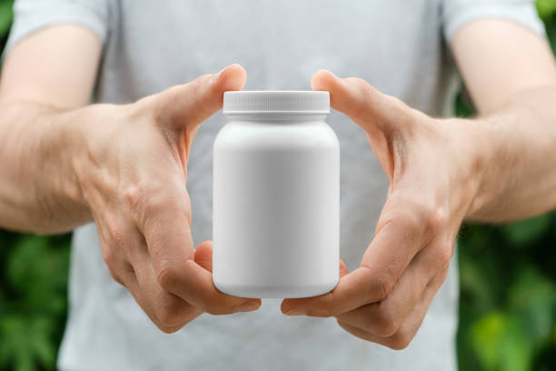 istock Man in a gray t-shirt holding with both hands white plastic bottle. Close up, copy space, place for label or branding. 1401509821