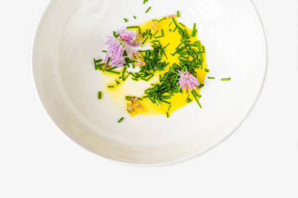 Sliced chive stem and violet blossoming chive flower with virgin vegetable oil in white plate on white background, closeup. Base for soup, use herb in cooking.