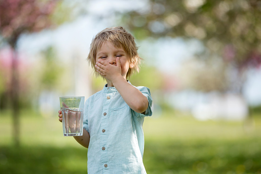 Beautiful blond child, boy, drinking water in the park on a hot summer day