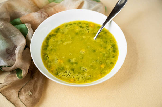 Pea and maize soup in white plate, spoon and scarf on yellow background,closeup.
