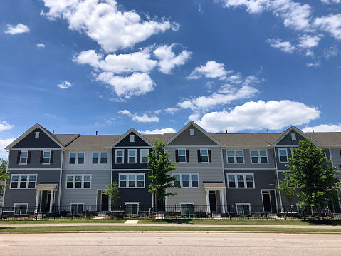 Multi-family home buildings made up of earth tone colored townhouses in Wake Forest, North Carolina USA. This image features a blue Carolina sky with white puffy clouds. Wake Forest is a suburb of Raleigh, NC.