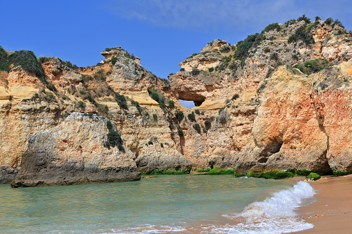 Sea stack and cliffs at the westernmost end of Praia da Prainha Beach with natural hole sculpted by the force of the sea waves and wind-caves carved at the cliff foot. Alvor Portimao-Algarve-Portugal.