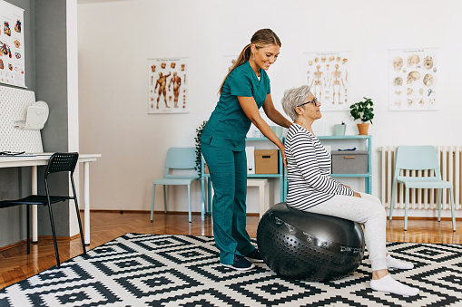 Senior woman sitting on the fitness ball and physiotherapist assisting with lumbal pain