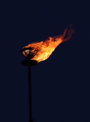 silhouetted hand holding a burning flaming torch over cloudy sky. 