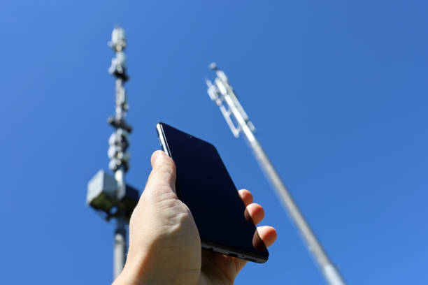 携帯電話基地局の背景にスマートフォンを持つ男性の手 - tower communications tower mobile phone antenna ストックフォトと画像