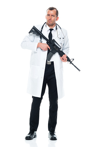 Front view of aged 40-44 years old with short hair caucasian young male doctor standing in front of white background wearing lab coat who is angry who is violence and holding weapon and using semi-automatic pistol