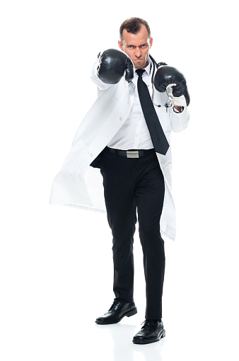 Full length of aged 40-44 years old with short hair caucasian young male doctor standing in front of white background wearing glove who is serious and boxing and showing fist who is in fighting stance