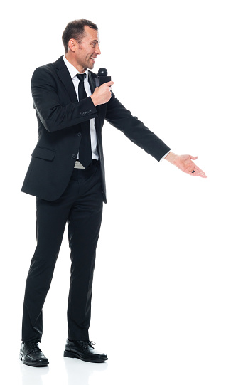 Full length of aged 40-44 years old with short hair caucasian young male public speaker standing in front of white background wearing businesswear who is giving speech who is showing with hand presenting and holding microphone