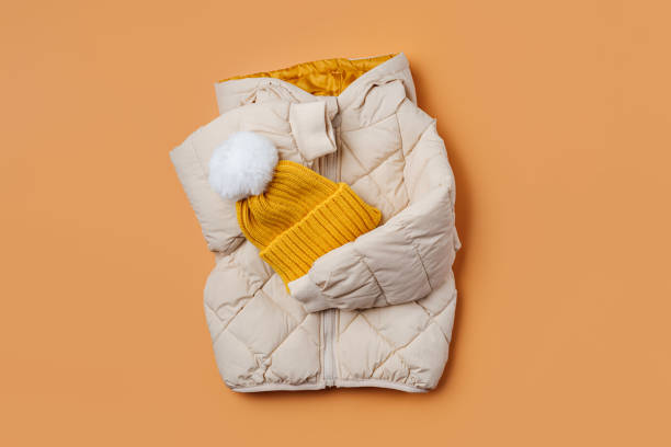オレンジ色の背景に黄色の帽子をかぶった子供用の暖かいフグジャケット。スタイリッシュな子供用アウターウェア。冬のファッション衣装 - coat ストックフォトと画像