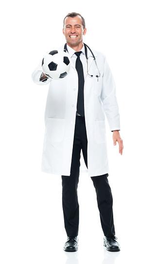 Front view of aged 40-44 years old with brown hair caucasian male doctor standing in front of white background wearing lab coat who is cheerful and holding soccer ball and using sports ball
