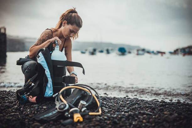 ウェットスーツの女性ダイバーが水に入る前に酸素タンクを準備する - oxygen tank underwater diving diving wetsuit ストックフォトと画像